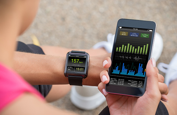 Woman in pink top looking at fitness stats on her smart watch and phone.